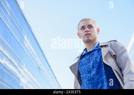 jeune homme d'affaires gay aux cheveux blonds courts, entrepreneur debout à l'extérieur des bâtiments de travail regardant et pensant, porte des vêtements formels, veste et shi Banque D'Images