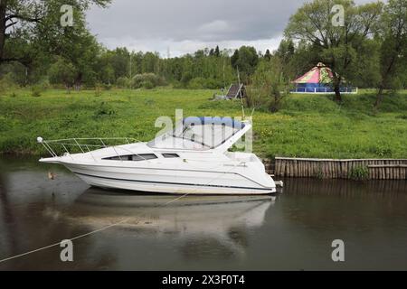 Petit bateau à moteur blanc amarré pendant la journée de pluie près du camp en été Banque D'Images