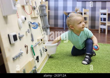 Petite fille joue sur le tapis vert avec un conseil occupé dans la maternelle moderne Banque D'Images