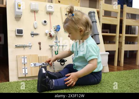 Petite fille joue sur le tapis avec un conseil occupé dans la maternelle moderne Banque D'Images