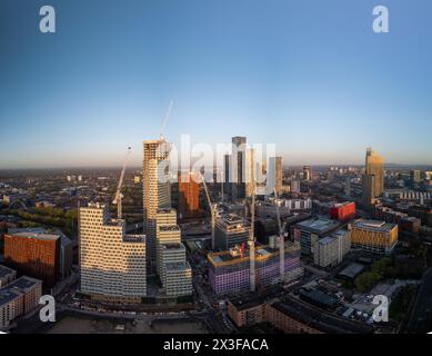 Une vue aérienne capturant les grues et les grues de construction d'une ville moderne baignées par la lueur chaude du soleil couchant Banque D'Images
