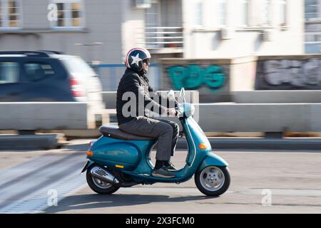 Belgrade, Serbie - 1er mars 2024 : un homme portant un casque vintage star jet chevauchant turquoise vespa scooter sur la rue de la ville, vue de profil Banque D'Images