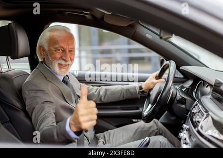 Un homme âgé en costume sourit avec l'approbation du siège du conducteur Banque D'Images