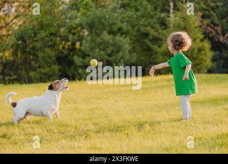 Petite fille joue avec un chien de compagnie sur la pelouse de jardin jetant une balle de jouet pour attraper Banque D'Images