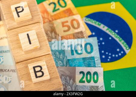 Le mot PIB (produit intérieur brut) écrit sur des cubes en bois avec de l'argent réel brésilien en jaune, drapeau vert du Brésil. Langue portugaise brésilienne Banque D'Images