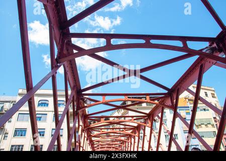 Pont en acier traversant la rivière dans la ville. Passage piétonnier avec toit, détail de construction de poutres métalliques rouges et structures de boulons. Banque D'Images