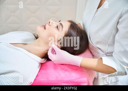 Jeune femme recevant un massage relaxant de l'oreille dans le centre de bien-être Banque D'Images