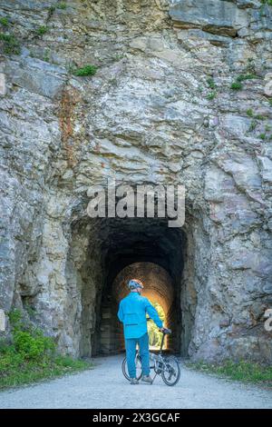 Cycliste masculin avec un vélo pliant sur Katy Trail dans un tunnel près de Rocheport, Missouri, paysage printanier. Le Katy Trail est une piste cyclable de 237 miles convertie f Banque D'Images