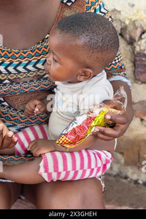 village jeune mère africaine nourrissant le bébé quelques collations Banque D'Images