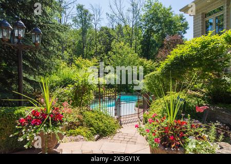 Piscine extérieure entourée de fer forgé couleur cuivre metal clôture de sécurité et diverses plantes vivaces, arbustes et arbres en arrière-cour de Banque D'Images