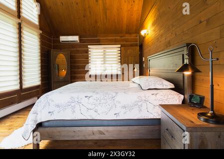Lit king size sur cadre en bois avec tête de lit en bois, table de nuit avec lampe de style industriel antique, commode avec miroir ovale dans la chambre principale à l'intérieur d'un Banque D'Images