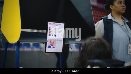 ZAPORIZHYA, UKRAINE - 15 MARS 2024 : électrice, femme avec SMA dans les votes en fauteuil roulant dans l'isoloir au bureau de vote. Un citoyen AMÉRICAIN handicapé utilise une tablette pour voter. Election présidentielle aux États-Unis d'Amérique. Banque D'Images