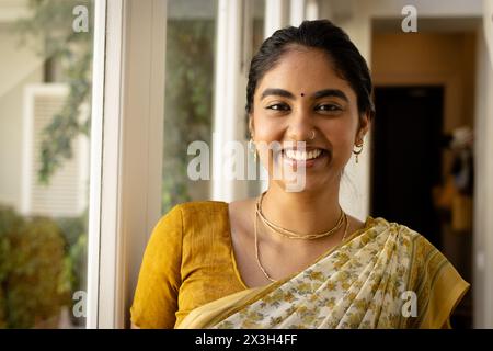 Jeune femme indienne portant le saree jaune traditionnel, souriant à la maison Banque D'Images