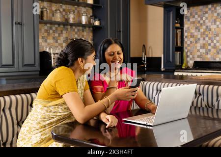 Mère indienne et fille riant à la maison avec un ordinateur portable Banque D'Images