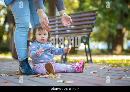 Bébé fille s'installant dans le parc et levant vos mains pour être levé Banque D'Images