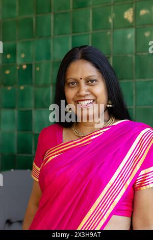 Une femme indienne d'âge moyen portant un saree rose vif, souriant à la maison Banque D'Images