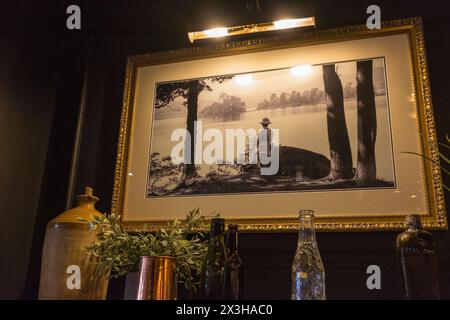 Photographie sur le mur d'une dame dans un chapeau regardant au-dessus d'un lac. Banque D'Images