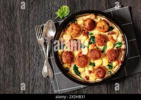 boulettes de poulet toscane avec gnocchi en sauce crémeuse avec tomates séchées au soleil et feuilles d'épinards dans un plat de cuisson sur une table en bois foncé avec fourchette et spo Banque D'Images