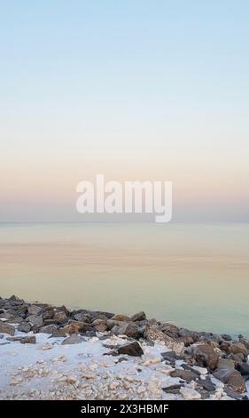 La lumière du coucher de soleil illumine doucement un littoral paisible. Un tas de rochers borde les eaux tranquilles qui s'étendent à l'horizon Dongying/China Banque D'Images