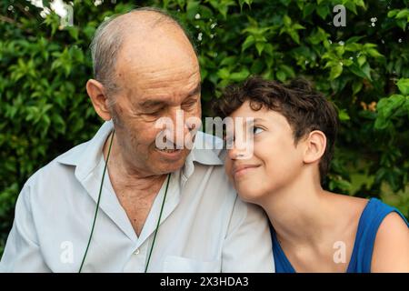 Grand-père et petit-fils profitant d'un rire partagé dans un jardin serein - un homme âgé et un jeune garçon regardant dans un moment tendre, entouré de verdure luxuriante Banque D'Images