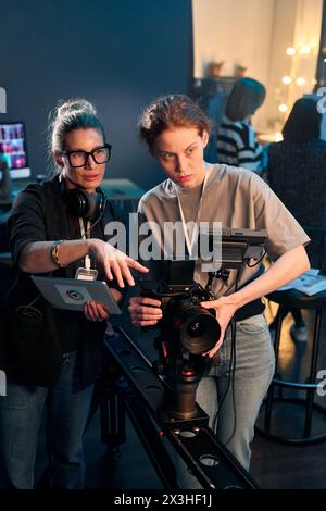 Portrait vertical de camerawoman exploitant la caméra vidéo professionnelle sur la plate-forme avec directrice féminine donnant des instructions Banque D'Images