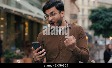 Heureux espoir heureux Indien arabe heureux homme ethnique homme d'affaires homme d'affaires homme jeune étudiant de sexe masculin tenir téléphone mobile smartphone souhaitant espoir prier les doigts croisés Banque D'Images
