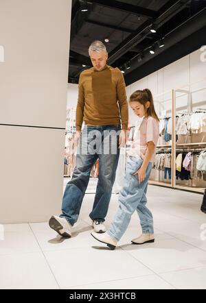 une petite fille essaie des chaussures avec son père dans un magasin. Banque D'Images