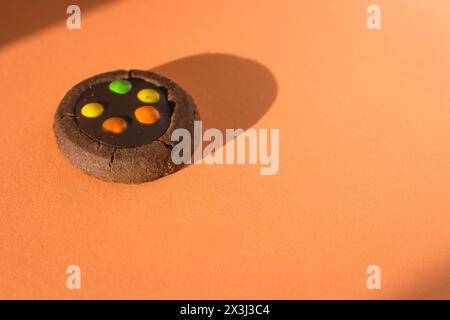 Biscuit brun avec des gouttes colorées sur fond de fuzz pêche. Biscuit au chocolat à la lumière du soleil sur fond orange. Dessert isolé avec espace copie. Banque D'Images