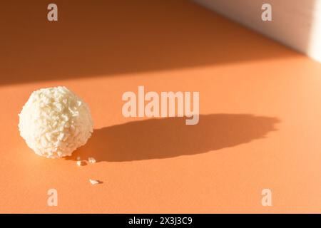 Bonbons crémeux sur fond de fuzz pêche. Noix de coco raffaello sur bannière de couleur pêche. Boule de Raffaello au soleil. Concept de simplicité. Dessert sucré isolé Banque D'Images