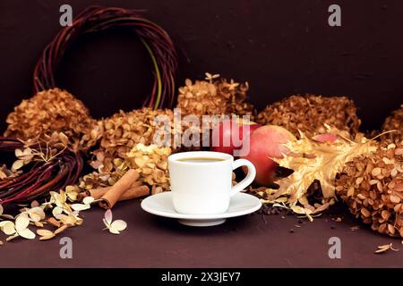 Tasse à café blanche avec expresso, cannelle, pommes rouges et hortensia sèche sur fond brun foncé. composition d'automne Banque D'Images
