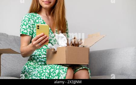 Femme déballe sa commande en ligne et prend des photos de ses achats. La personne féminine partage des critiques du service de livraison en ligne. E-commerce. Banque D'Images