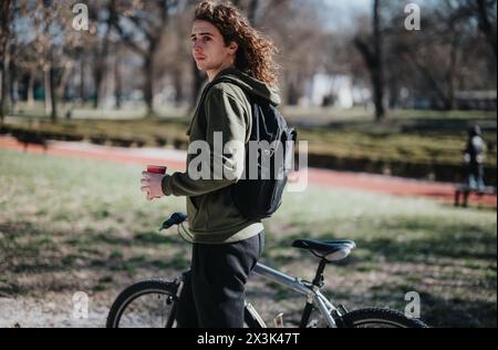 Jeune homme tenant une tasse de café en pause lors d'une balade à vélo dans le parc par une journée ensoleillée Banque D'Images