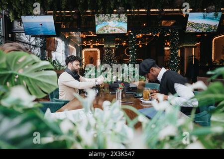 Deux jeunes professionnels travaillent ensemble dans un café urbain élégant entouré d'une verdure vibrante et d'un décor moderne. Banque D'Images