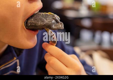 le jeune garçon mord une boulette noire dans une fourchette. Nourriture nationale Banque D'Images