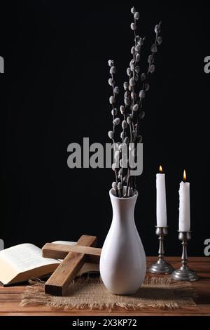Bougies d'église brûlantes, croix, Bible et vase de branches de saule sur une table en bois Banque D'Images