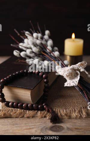 Perles de Rosaire, Bible, bougie allumée et branches de saule sur la table en bois, gros plan Banque D'Images