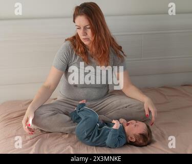 Une femme caucasienne est assise sur un lit à côté d'un bébé qui pleure. Dépression du post-partum. Banque D'Images
