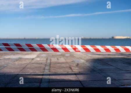 une corde rayée rouge et blanche repose sur le sol. La corde est sur une plage près de l'eau. Banque D'Images