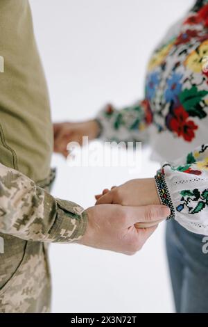 Mariée en chemise brodée nationale ukrainienne et marié en uniforme militaire se tiennent les uns les autres par les mains. Gros plan. La notion de mariage en temps de guerre. WA Banque D'Images