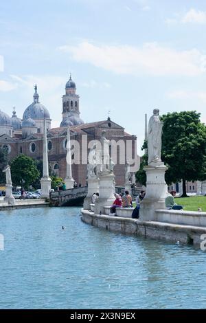 Journée ensoleillée à Prato della Valle avec des gens sur la rive du canal. L'île verte centrale, Memia, entourée de statues. En vue de la basilique abbatiale de sa Banque D'Images