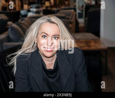 Femme professionnelle confiante avec des cheveux blonds platine dans un Blazer noir chic souriant au magasin de meubles Banque D'Images