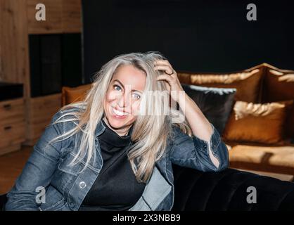 Femme mature contemplative se prélassant dans une pièce sombre avec un éclairage doux, un regard réfléchi dans ses cheveux blonds platine Banque D'Images