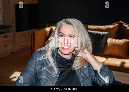 Femme mature contemplative se prélassant dans une pièce sombre avec un éclairage doux, un regard réfléchi dans ses cheveux blonds platine Banque D'Images