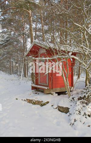 Petit WC extérieur en bois peint en rouge dans la forêt en hiver avec de la neige sur le sol, Porkkalanniemi, Kirkkonummi, Finlande. Banque D'Images