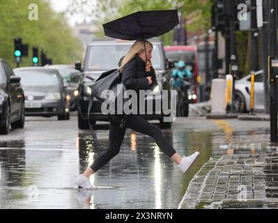 Les piétons sautent au-dessus d'un bassin d'eau de pluie qui s'est accumulé sur la section ouest de la route Euston, adjacente à la jonction avec Woburn place, Londres. Date de la photo : dimanche 28 avril 2024. Banque D'Images