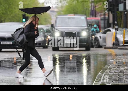 Les piétons sautent au-dessus d'un bassin d'eau de pluie qui s'est accumulé sur la section ouest de la route Euston, adjacente à la jonction avec Woburn place, Londres. Date de la photo : dimanche 28 avril 2024. Banque D'Images