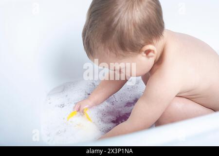 Gros plan des mains d'un petit enfant éclaboussant et jouant avec de l'eau dans la baignoire, mettant en valeur le pur plaisir et la curiosité. Banque D'Images