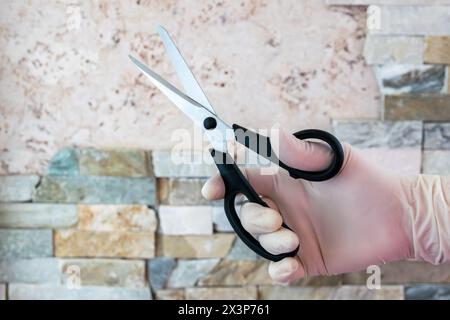 Ciseaux dans la main avec gant en caoutchouc. Cisaille en acier pour la coupe. Banque D'Images