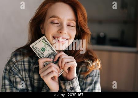 Gros plan portrait d'une femme indépendante heureuse tenant dans les mains un tas de dollars qu'elle gagnait tout en travaillant à distance à la maison. Revenus à distance, en ligne Banque D'Images