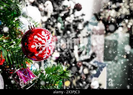 Sapin de Noël décoré avec une boule colorée sur fond flou de neige tombante de bokeh étincelant Banque D'Images